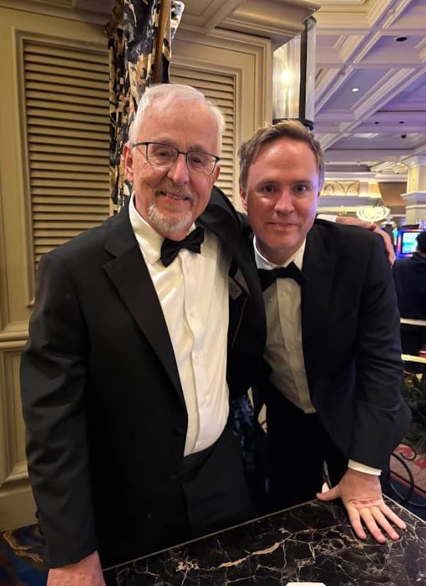 Prof. Richard Larson with a guest in tuxedos at a marble table during the IAOTP Vegas gala, 2025