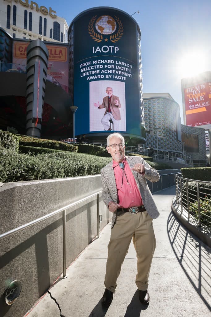 Prof. Larson in front of the IAOTP Planet Hollywood billboard in Las Vegas, 2025